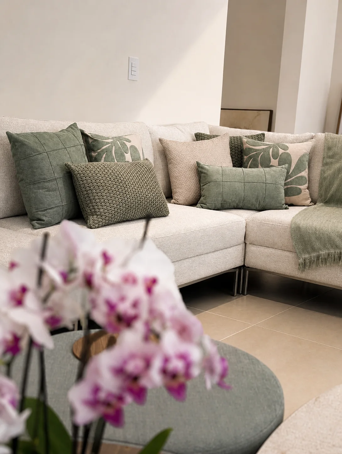 Sala com sofá, manta e almofadas coordenadas em verde, bege e marfim